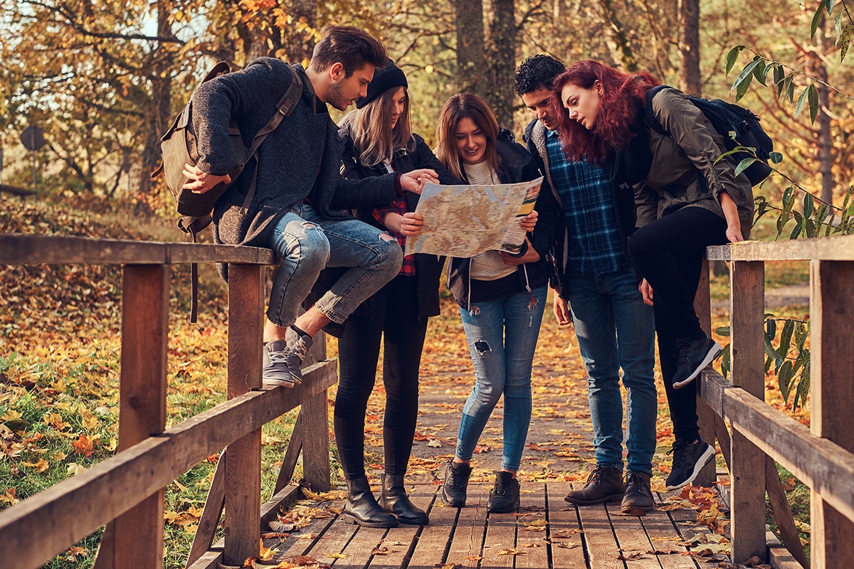 Travel, hiking, adventure concept. Group of young friends hiking in autumn colorful forest, looking at map and planning hike.
