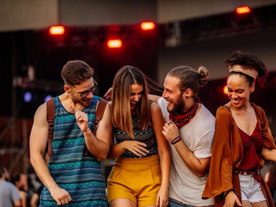 A perfect example of fan engagement, a group of diverse friends laughing and cheering together, enjoying live music and group experiences at a ticketed performing arts festival.
