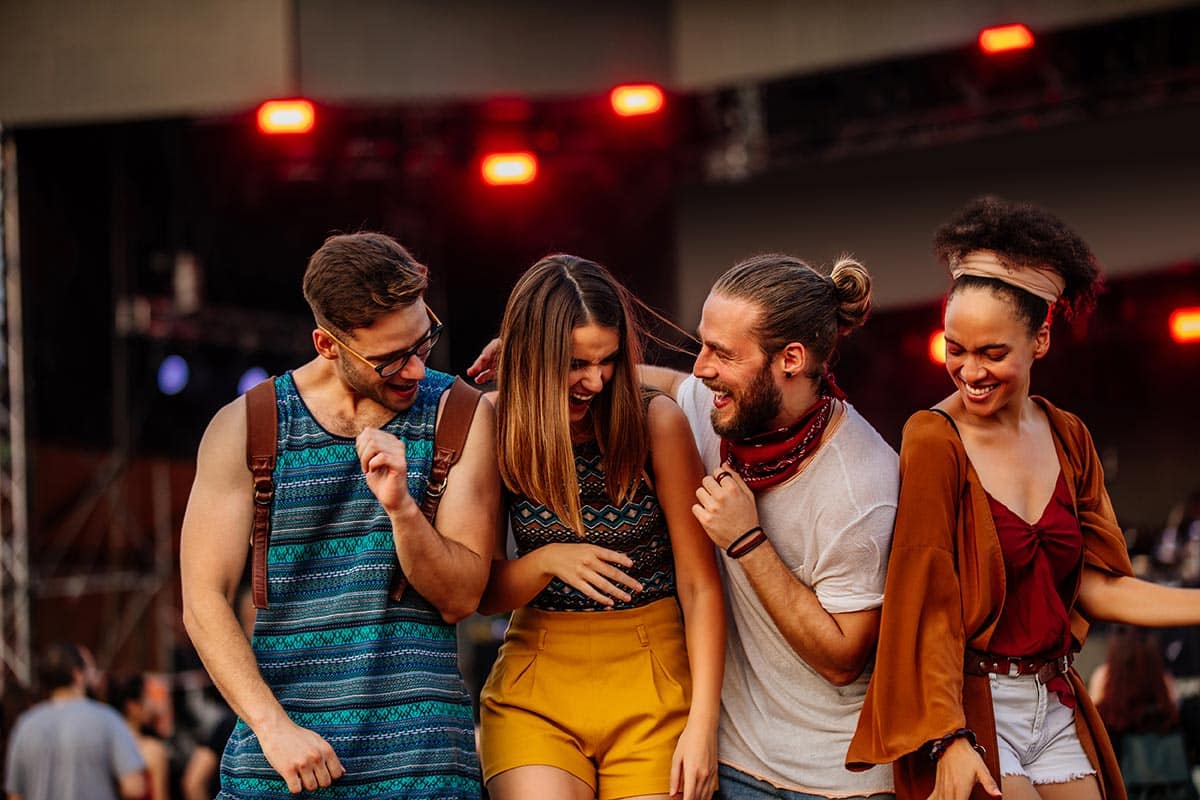 A perfect example of fan engagement, a group of diverse friends laughing and cheering together, enjoying live music and group experiences at a ticketed performing arts festival.